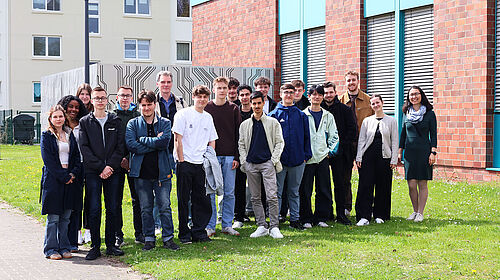 Schüler:innen beim Ideenwettbewerb an der Hochschule Wismar Gruppe von Schülerinnen und Schülern steht gemeinsam mit Lehrenden vor einem Hochschulgebäude auf einer Grünfläche.