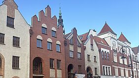 Eine Hausfassade mit historischen Gebäuden vor einem blauen Himmel.