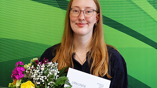 Lara Baumbach für Bachelorarbeit ausgezeichnet Lara Baumbach hält Urkunde und Blumenstrauß nach der Auszeichnung ihrer Bachelorarbeit.