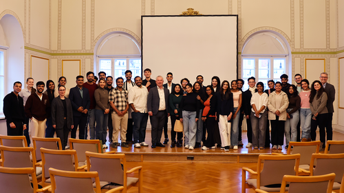 Gruppenfoto mit internationalen Studierenden im Rathaus Etwa 35 Personen stehen in einem hellen Saal vor einer Leinwand. In der Mitte der erste Reihe stehen Bürgermeister Beyer und die Studierenden, außen rechts Prof. Dr. Arnaout.