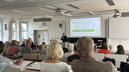 Digitale Pflege im Gespräch Volker Grienitz hält vor zahlreichen Teilnehmenden in einem Hörsaal einen Vortrag zur modernen Pflege.